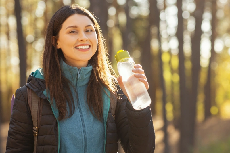 Young fit woman drinking water at the beach, understanding signs of dehydration